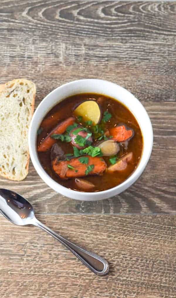 Not your average beef stew with carrots and bread on a wooden table.