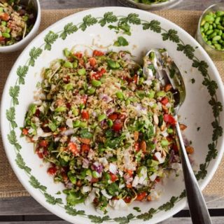 A refreshing summer bowl of California Quinoa Salad adorned with colorful vegetables, served alongside a handy spoon.