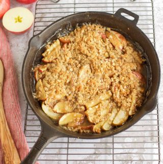 A gluten free apple crisp in a cast iron skillet on a cooling rack.