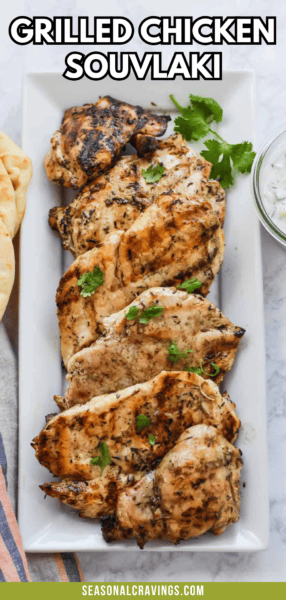 A rectangular white plate of grilled chicken souvlaki garnished with cilantro, next to pita bread and a bowl of tzatziki sauce. Text above reads "Grilled Chicken Souvlaki" and "seasonalcravinging.com". Enjoy the succulent flavors at Seasonal Craving.