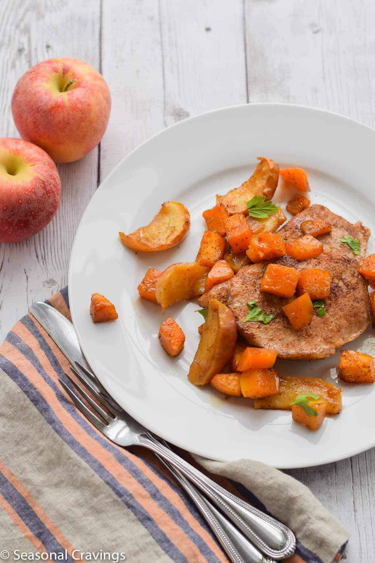 Sheet Pan Brown Sugar Pork Chops on a white plate with two apples on the side