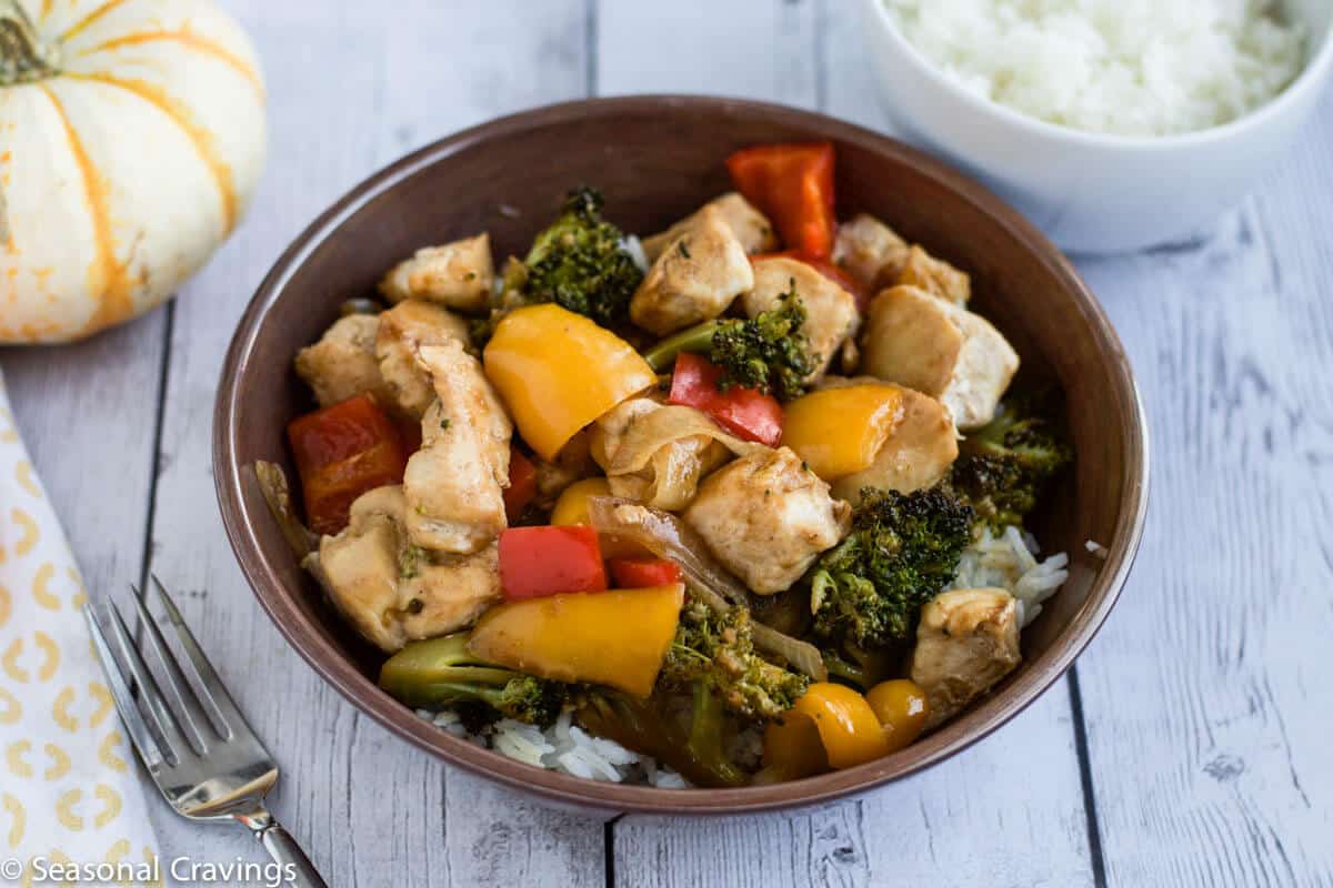 chicken stir fry in a brown bowl with pumpkins on side