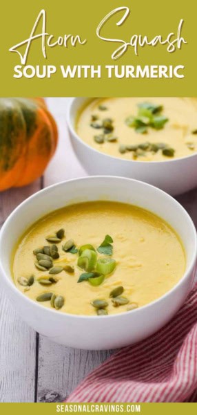 Two white bowls of acorn squash soup with turmeric, garnished with green onions and pumpkin seeds, rest on a white wooden surface beside an orange and green squash.