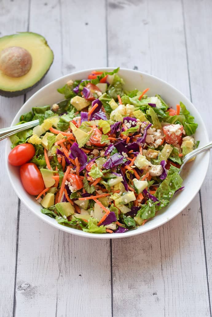 chopped salad with carrots, tomato and avocado in a white bowl