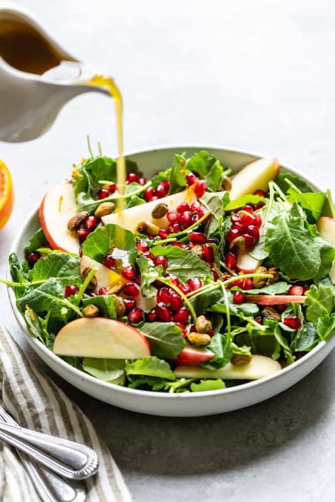 dressing being poured onto a kale salad