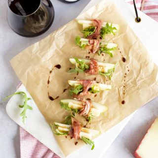 A plate with prosciutto wrapped pears, manchego, and a bottle of wine.