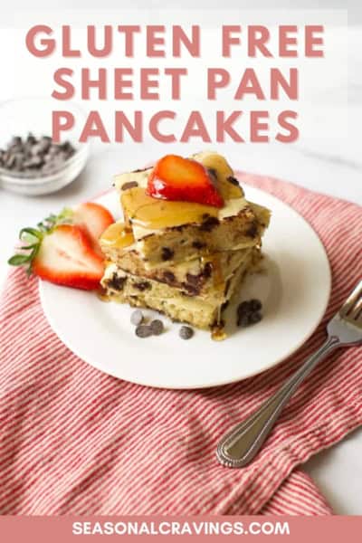 A plate with three square slices of gluten-free sheet pan pancakes topped with strawberries and syrup, placed on a red and white striped cloth next to a silver fork. Text reads "GLUTEN FREE SHEET PAN PANCAKES".