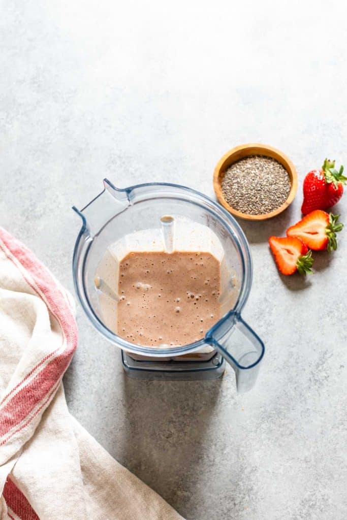 blender with strawberry smoothie and berries on the side