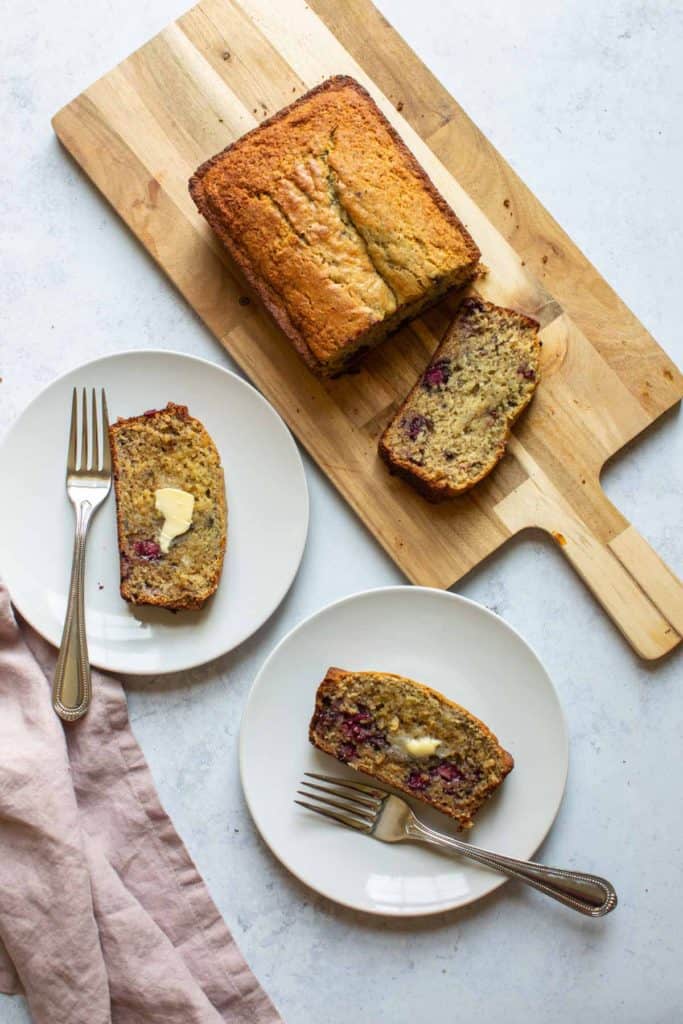 banana bread on a wooden board with two slices on white plates