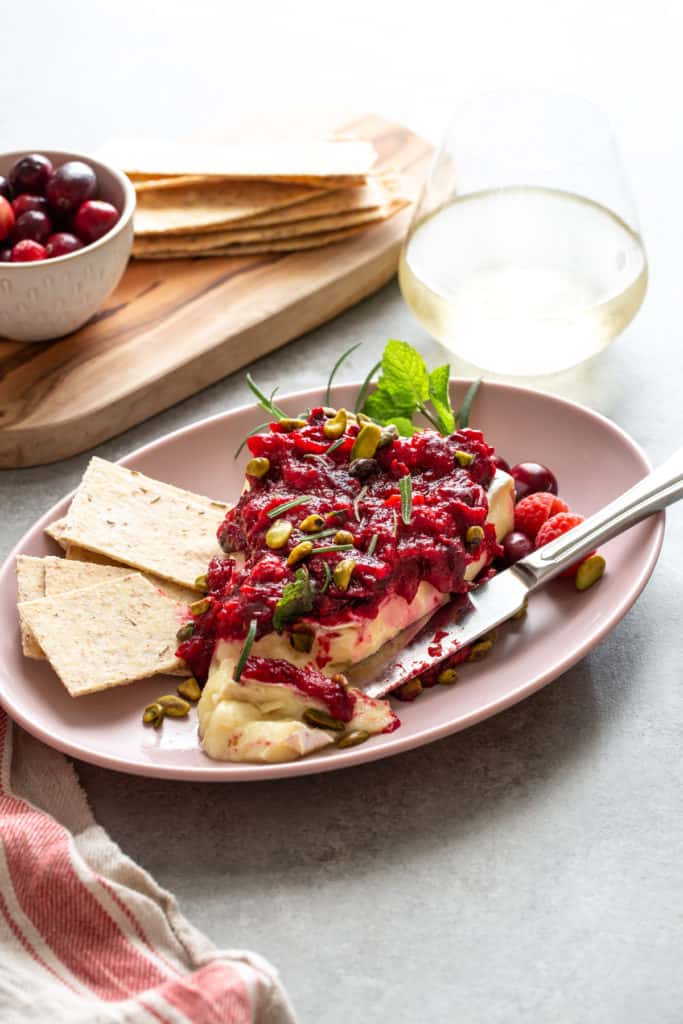 baked brie with raspberry sauce on a pink plate with crackers