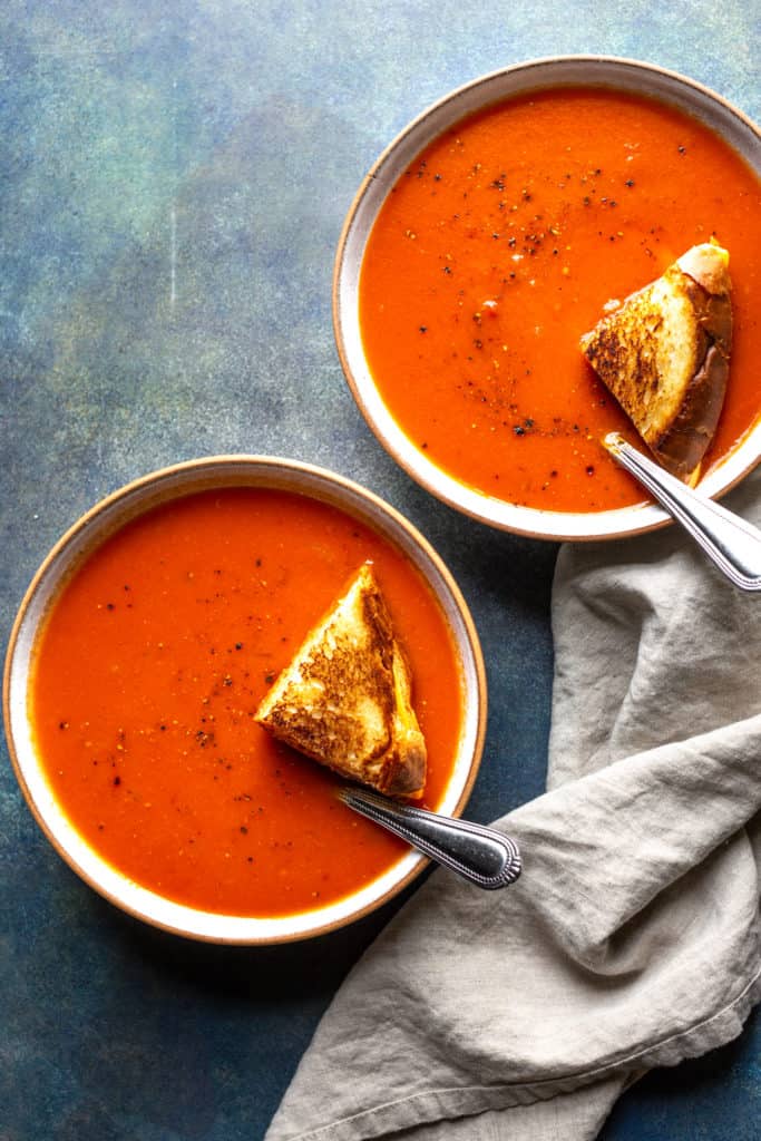 spicy tomato soup in two bowls with grilled cheese on top