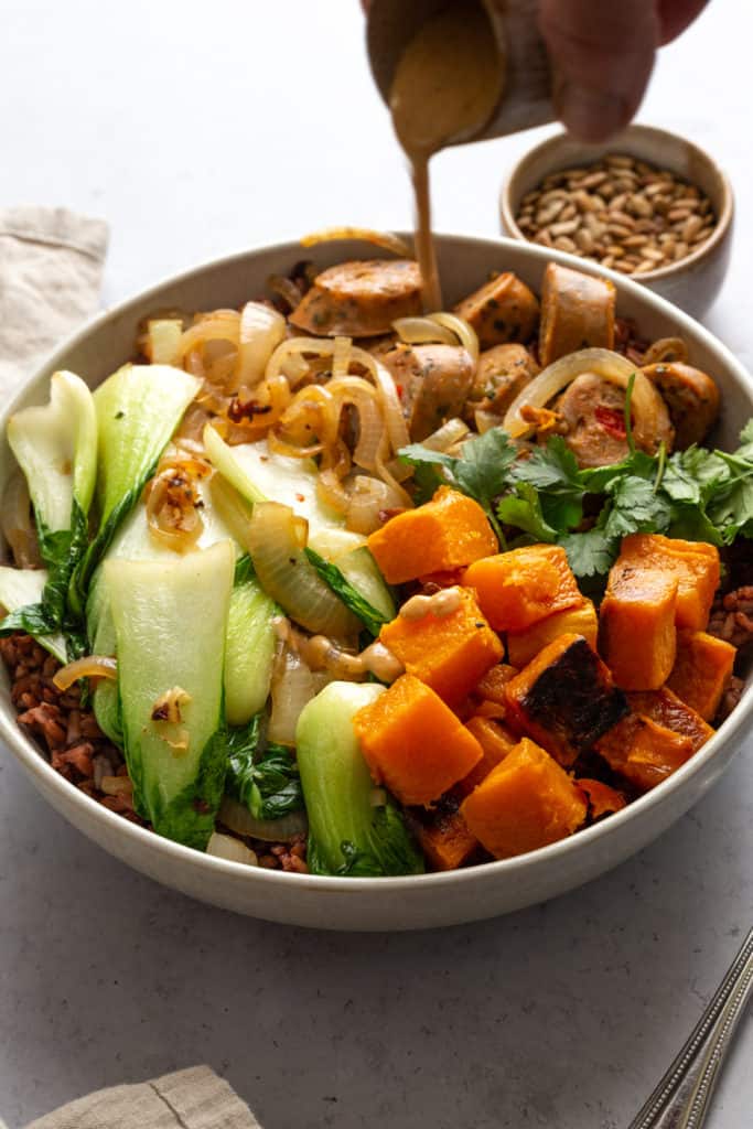 pouring tahini dressing on grain bowl