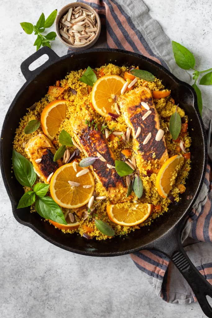 turmeric salmon and couscous with oranges in a black skillet