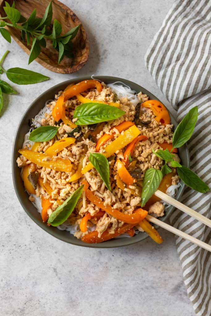 thai basil chicken with rice noodles and thai basil leaves on top and on the side