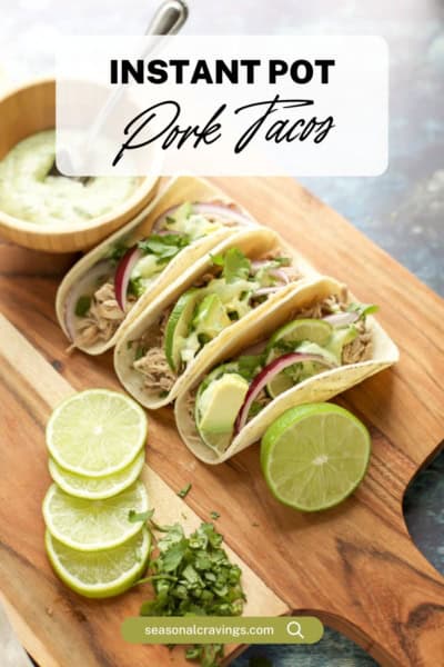 A wooden board with three Instant Pot pork tacos garnished with avocado slices, greens, lime halves, and a bowl of green sauce. The text "Instant Pot Pork Tacos" appears at the top.