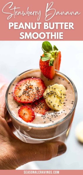 A hand holds a glass of strawberry banana peanut butter smoothie topped with banana slices, strawberry slices, and chia seeds. The text reads "Strawberry Banana Peanut Butter Smoothie.