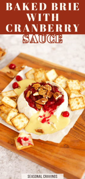 A round of baked brie cranberry delight topped with sauce and chopped pecans, surrounded by crackers on a wooden board. The text reads, "Baked Brie with Cranberry Sauce.