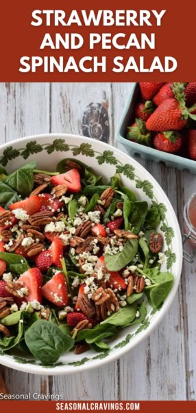 A bowl of strawberry and pecan spinach salad topped with strawberries, pecans, and feta cheese sits on a wooden table next to a box of fresh strawberries. Text on the image reads "Strawberry and Pecan Spinach Salad.