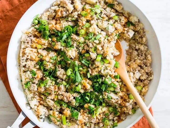 A skillet filled with cooked ground turkey, chopped vegetables, and fresh herbs with a wooden spoon resting on the side.