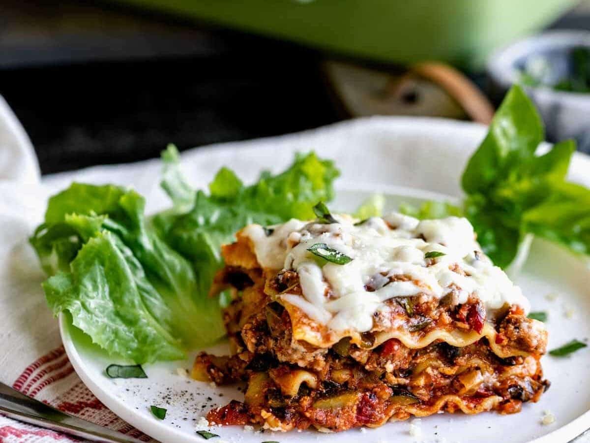 A plate of vegetable lasagna garnished with fresh basil and served with a side of lettuce.