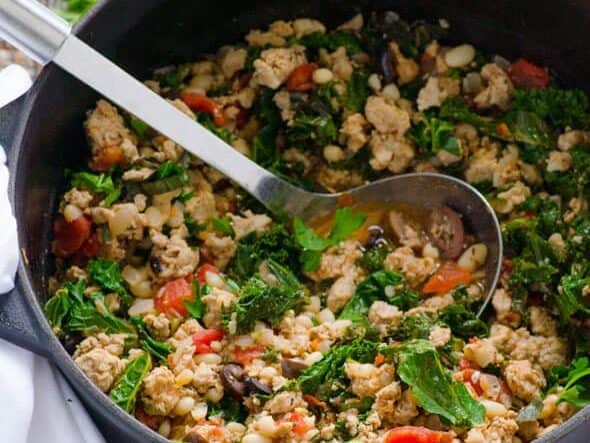 A skillet filled with a sautéed mix of chopped vegetables, beans, and ground meat or tofu, with a metal spoon resting on the side.