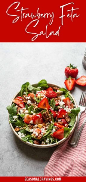 A salad with fresh strawberries, feta cheese, pecans, and leafy greens is served in a bowl. Sliced strawberries and a fork are placed next to the bowl. The text "Kale and Strawberry Feta Salad" is at the top.