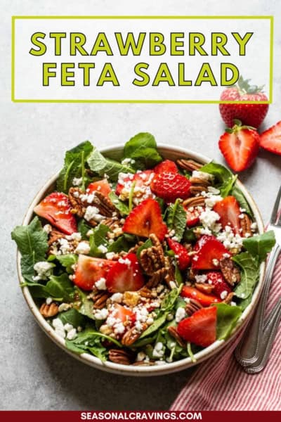 A bowl of kale and strawberry salad with spinach, pecans, and feta cheese on a gray surface. Text above the bowl reads "Strawberry Feta Salad".