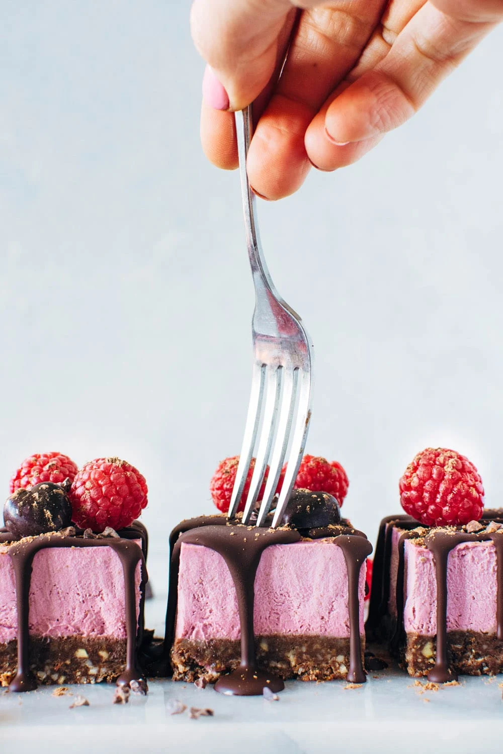 An individual indulging in a slice of gluten-free chocolate raspberry cheesecake.