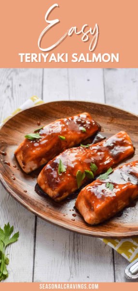 Three pieces of teriyaki-glazed salmon are arranged on a wooden plate, garnished with green herbs. Text at the top reads "Teriyaki Salmon in Oven," with a web address "seasonalcravinging.COM" at the bottom.