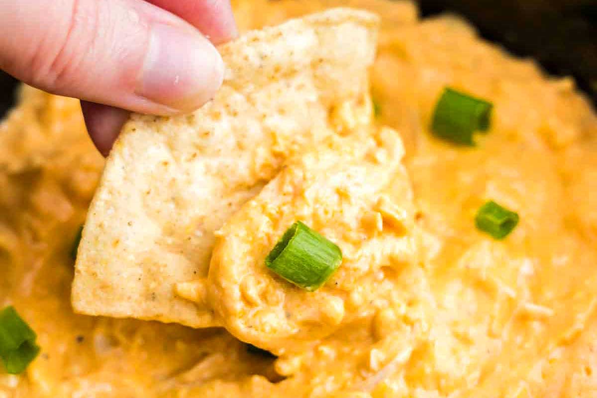 A person dipping a tortilla into a bowl of buffalo chicken dip.