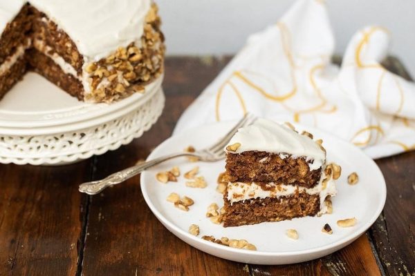 A slice of carrot cake with icing and walnuts on a plate.