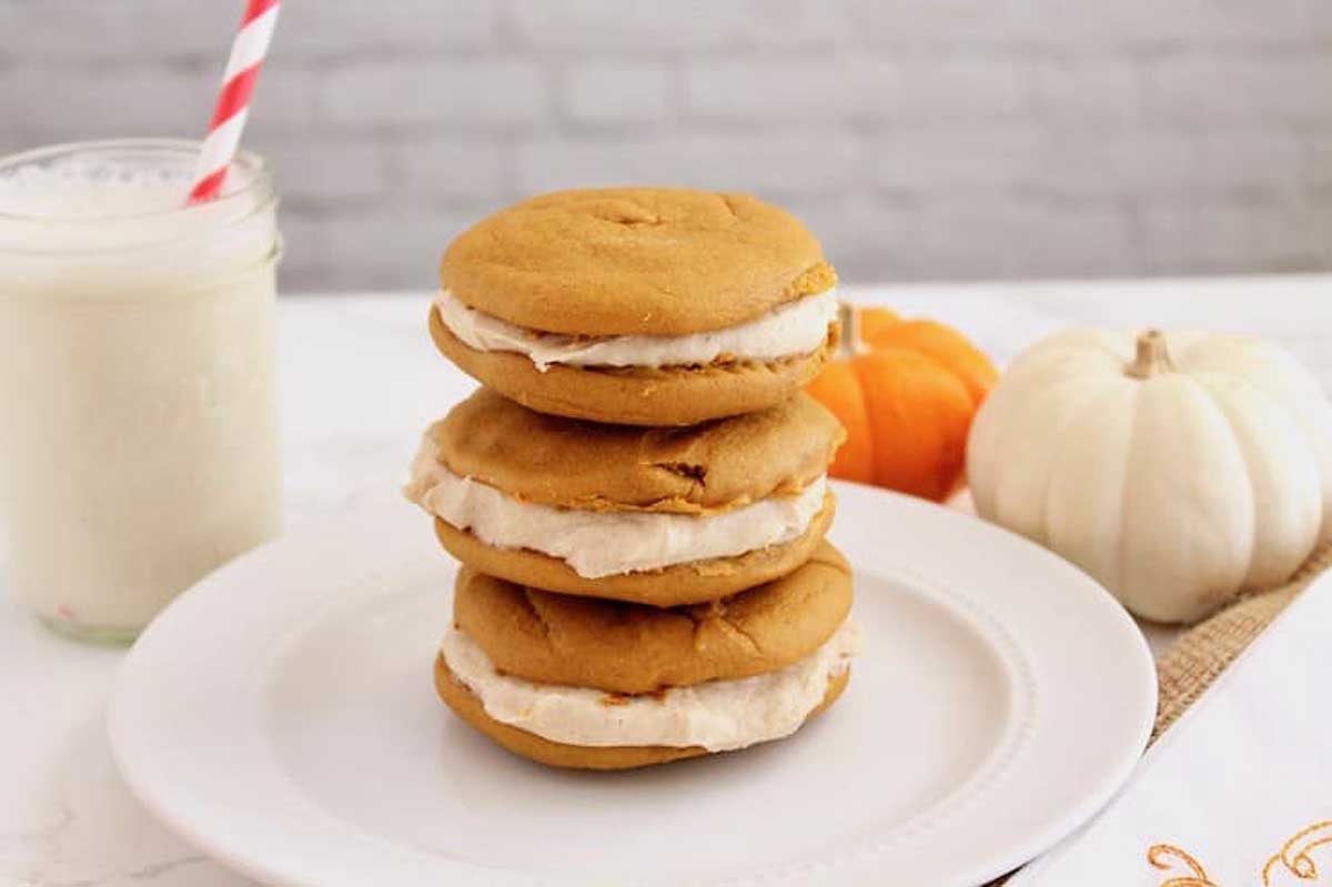 A stack of pumpkin ice cream sandwiches on a plate next to a glass of milk.