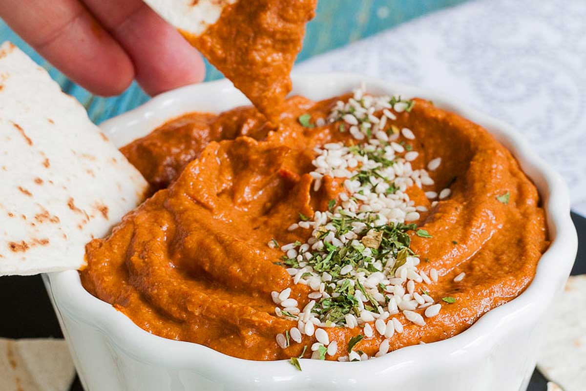 A person is dipping a tortilla into a bowl of hummus.