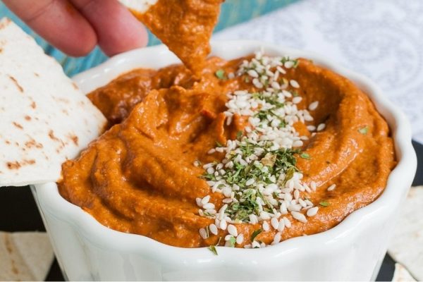 A person is dipping a tortilla into a bowl of hummus.