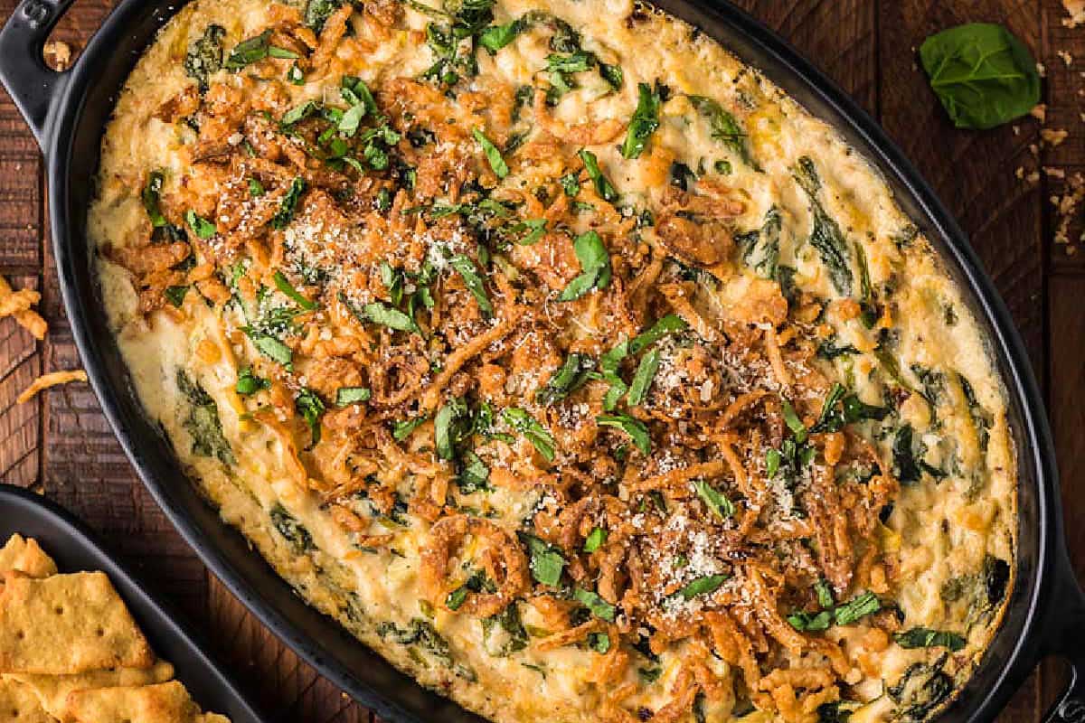 Cheesy spinach dip in a cast iron skillet with crackers.