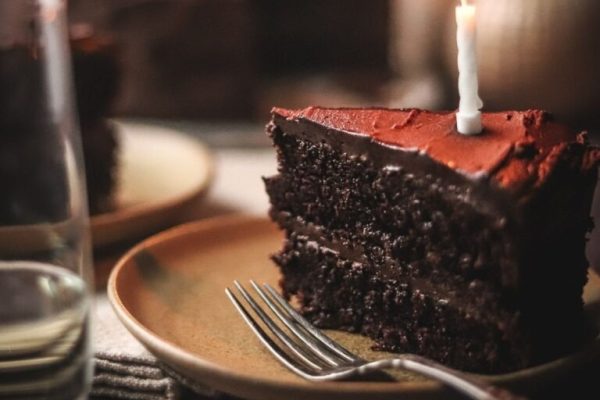 A slice of chocolate cake on a plate with a candle.