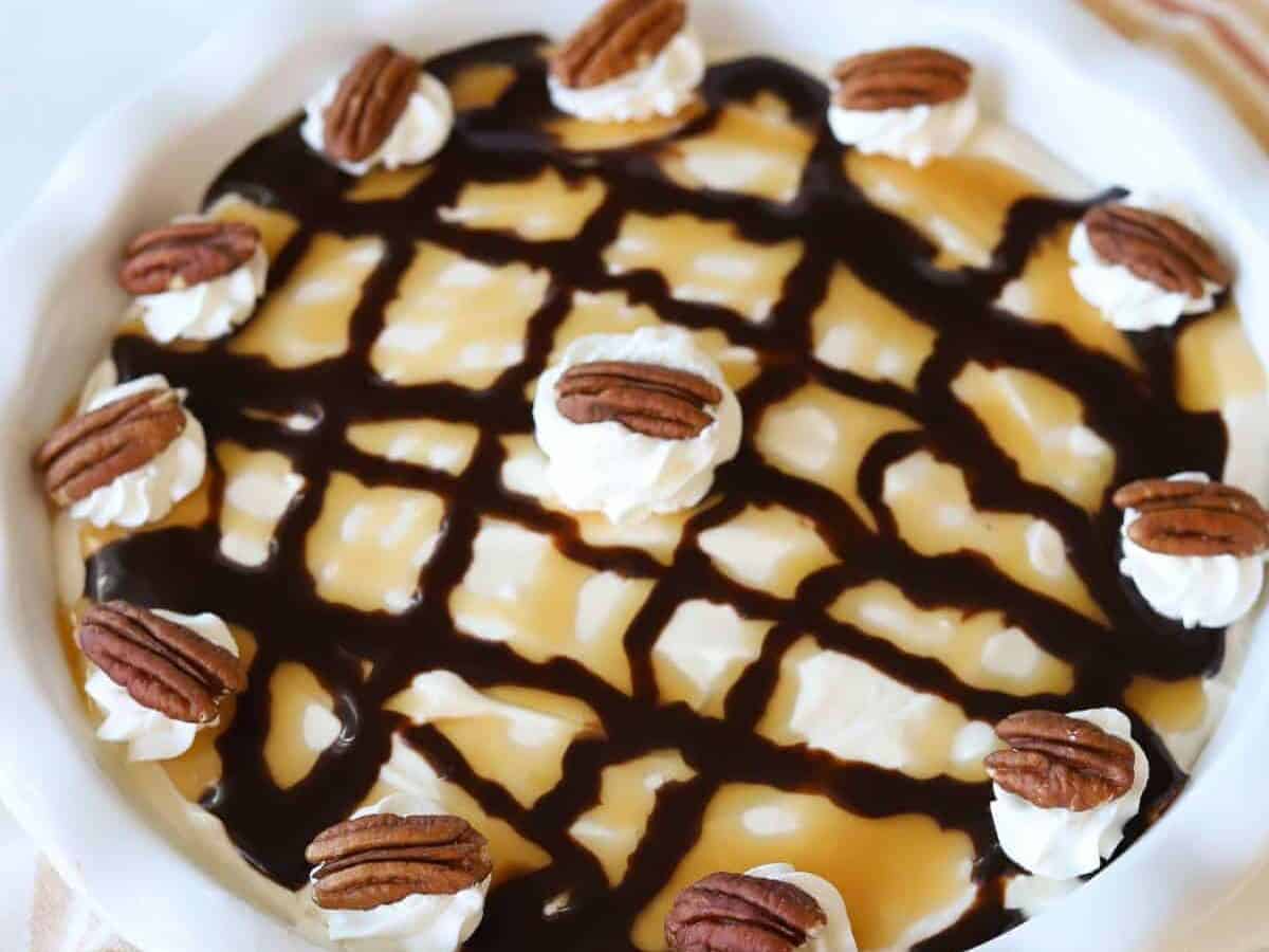 Turtle pie in a round baking dish topped with pecans and cream.