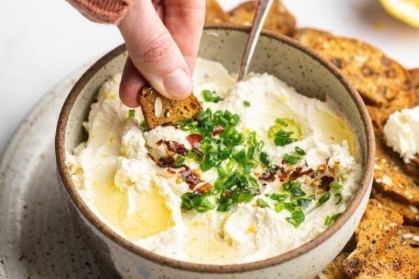 A person dipping a spoon into a bowl of hummus.