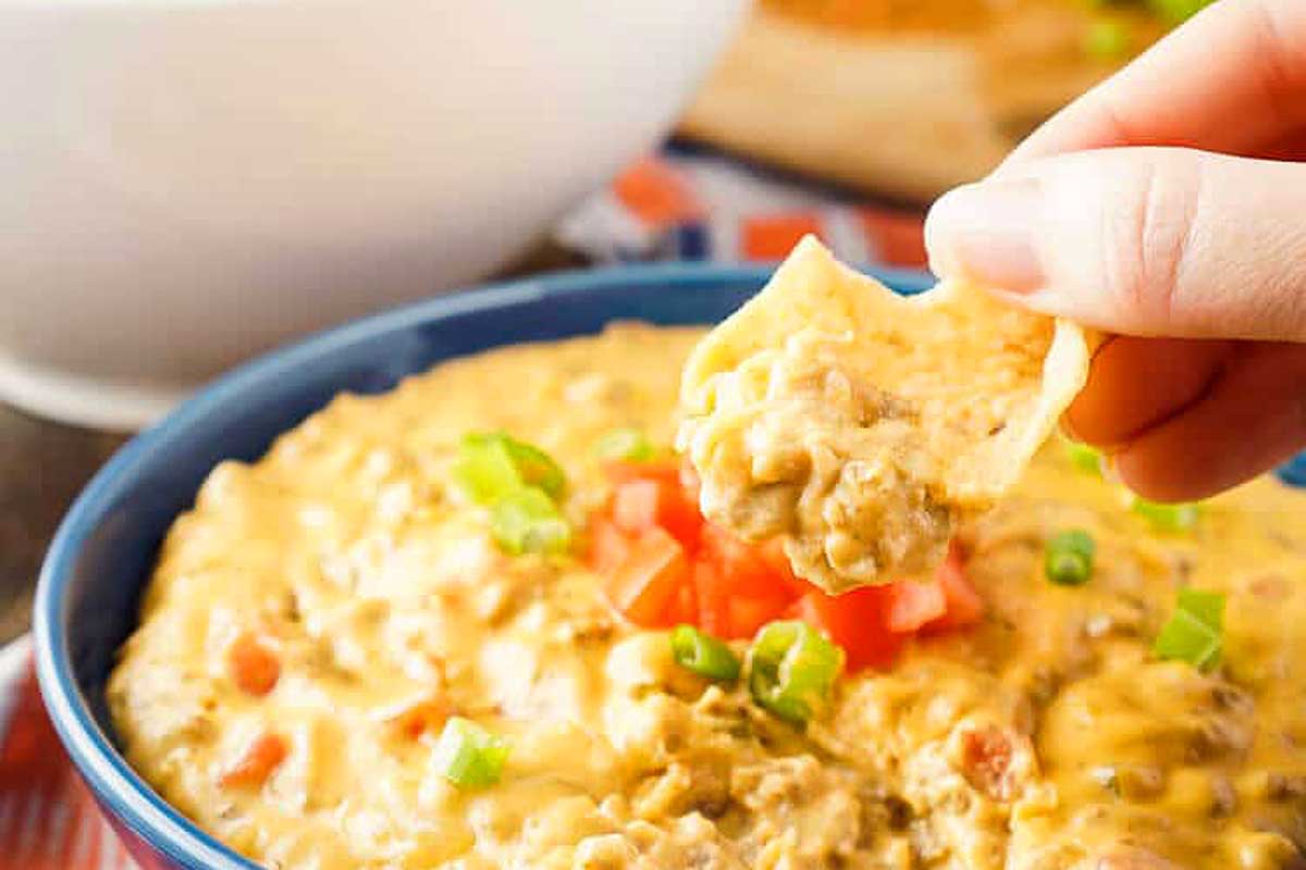 A person dipping a tortilla into a bowl of cheese dip.