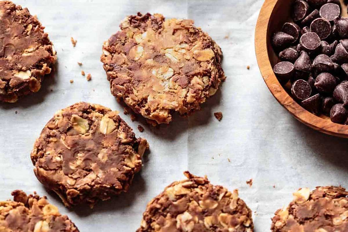 A bowl of chocolate chips next to a plate of cookies.