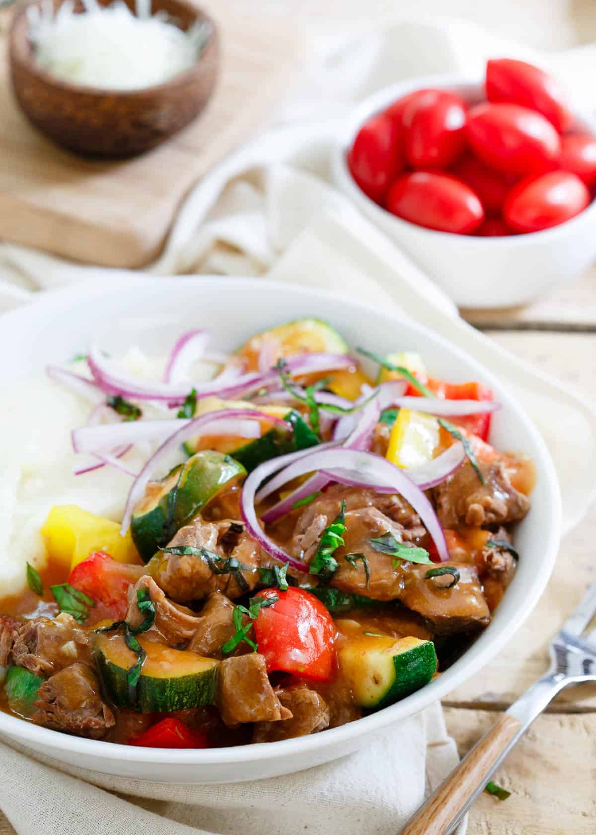 A white bowl with chuck steak and vegetables in it.