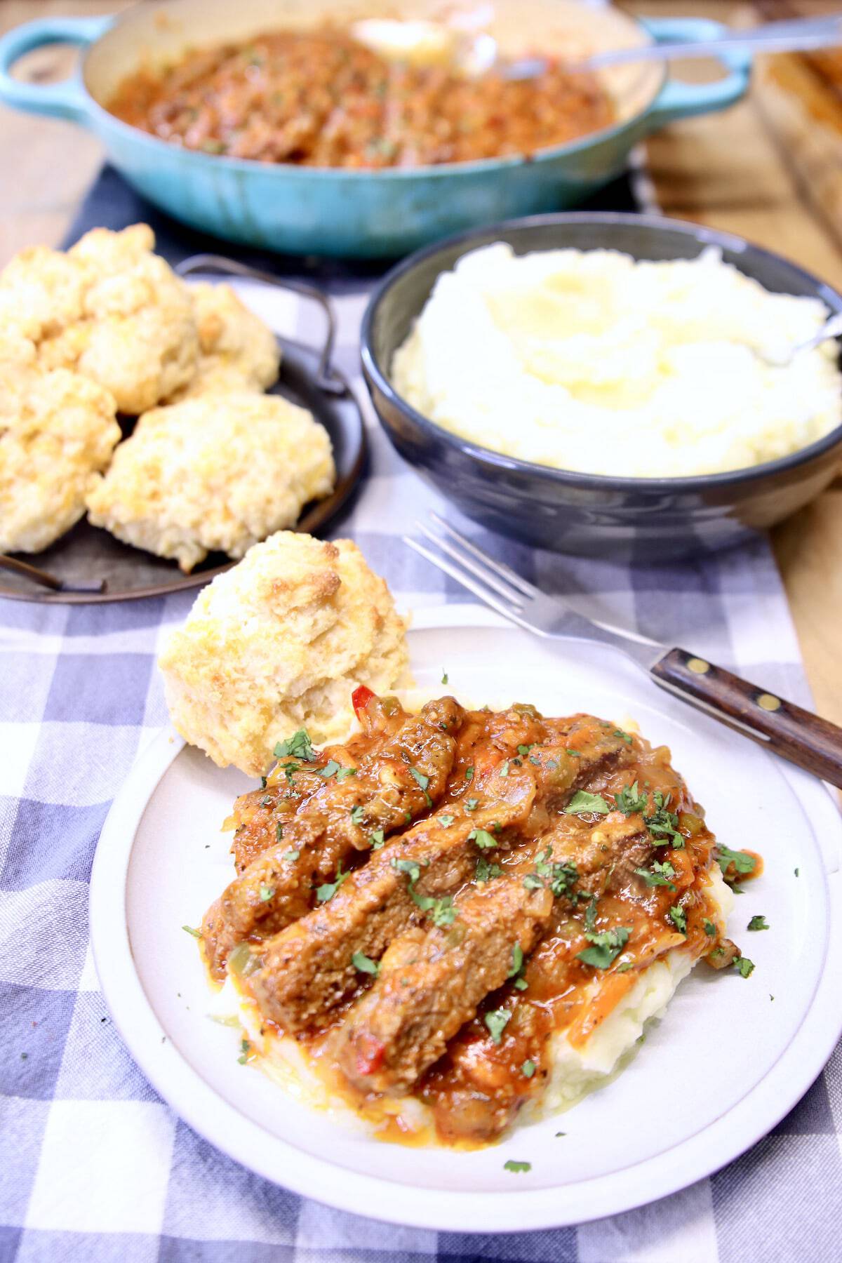 A plate with chuck steak, mashed potatoes and biscuits.