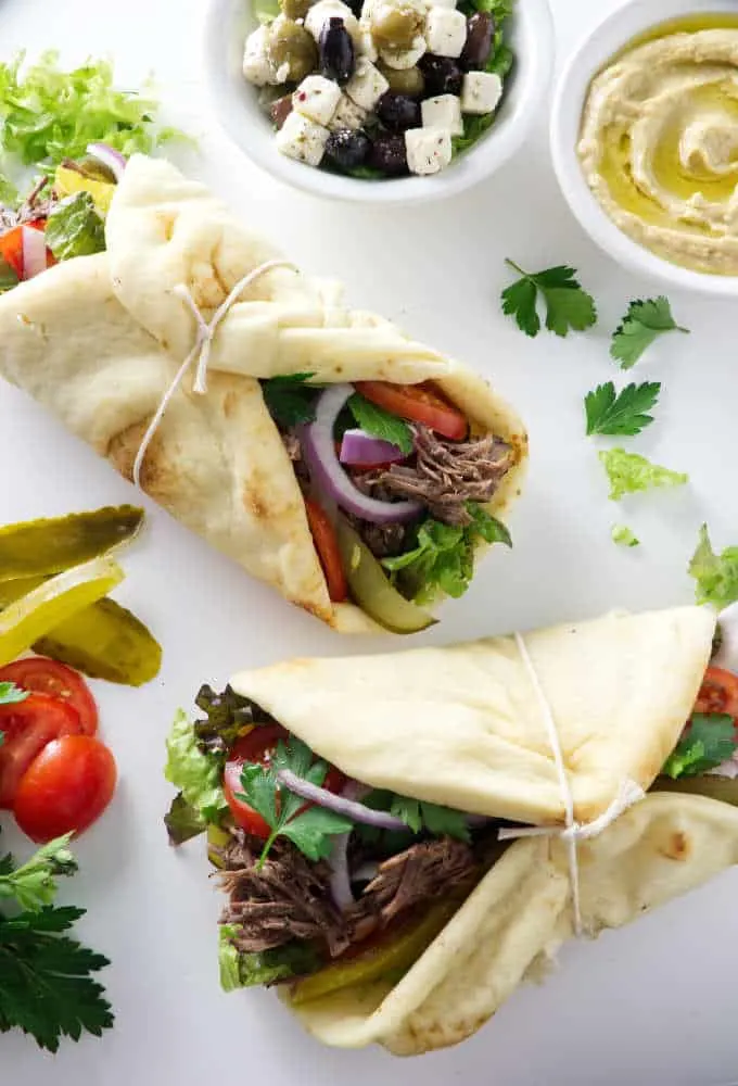 Two pitas with chuck steak and vegetables on a white plate.