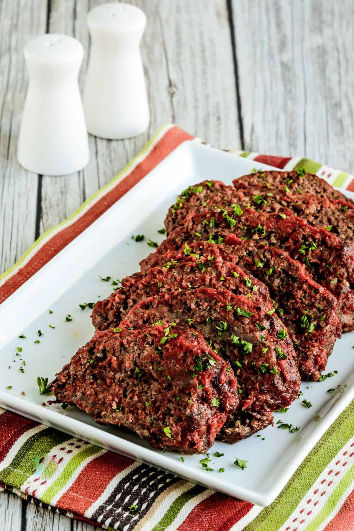 Beef and Sausage Italian Meatloaf on serving plate with salt and pepper in background. 
