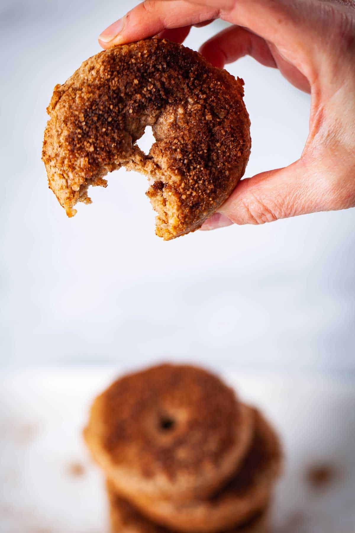 A person holding a unique cinnamon donut with a bite taken out of it.