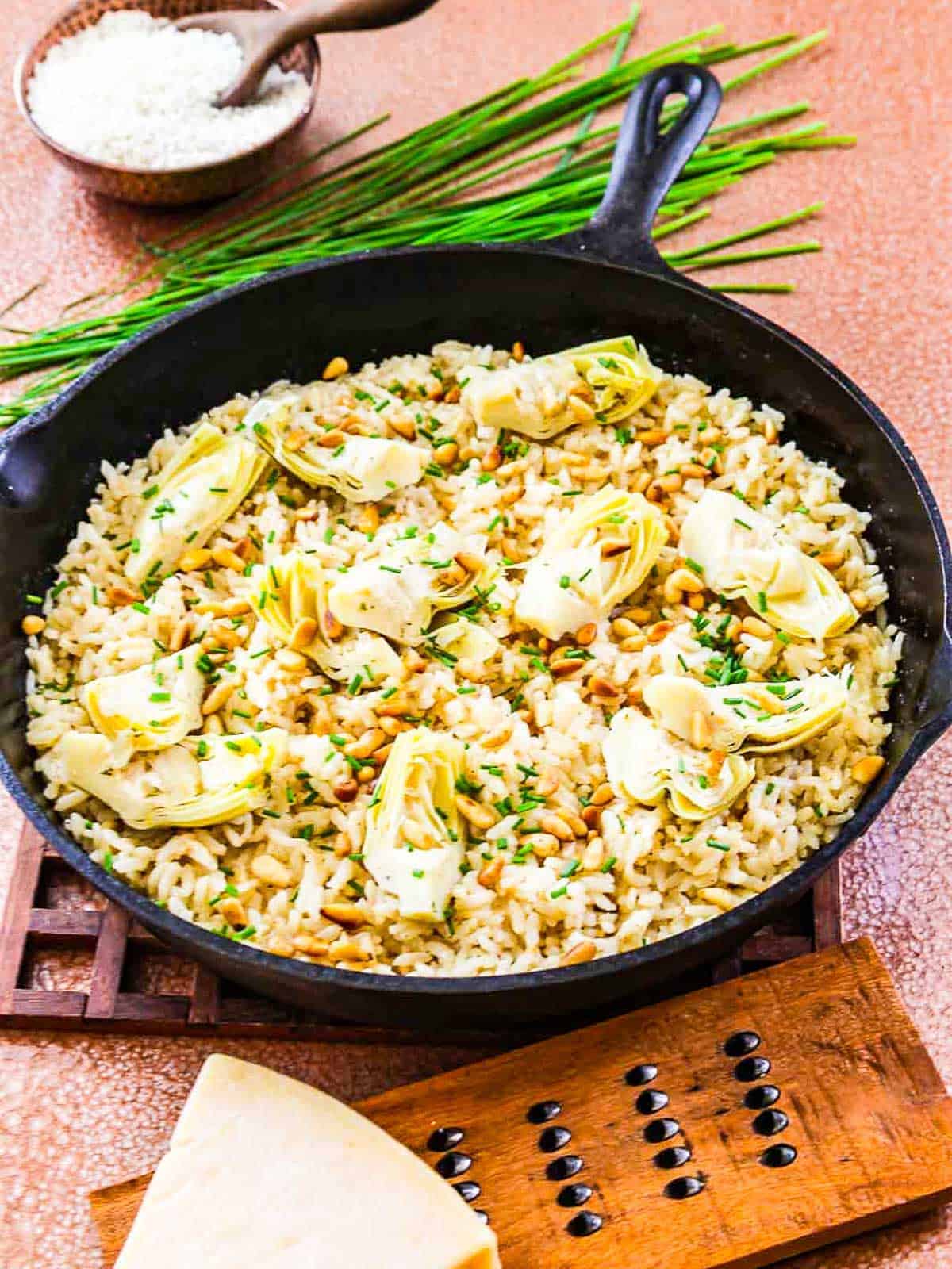 A pan of risotto on a wood hot pad on a table. 
