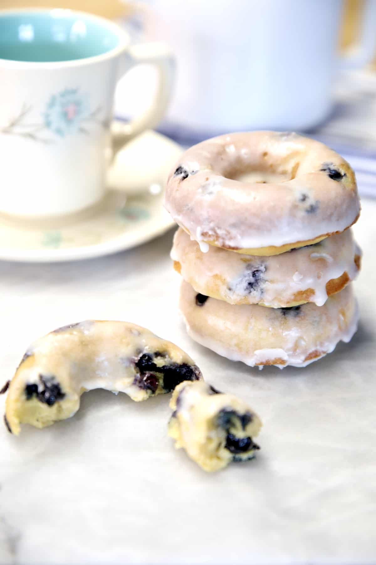 A stack of unique blueberry donuts on a table next to a cup of coffee.