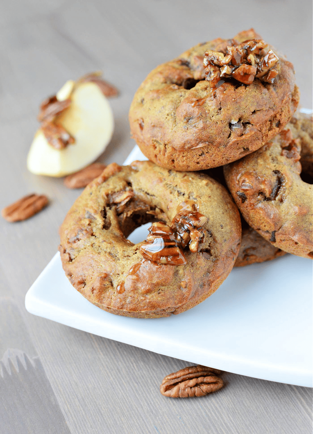 A stack of unique donuts with pecans and apples on a white plate.