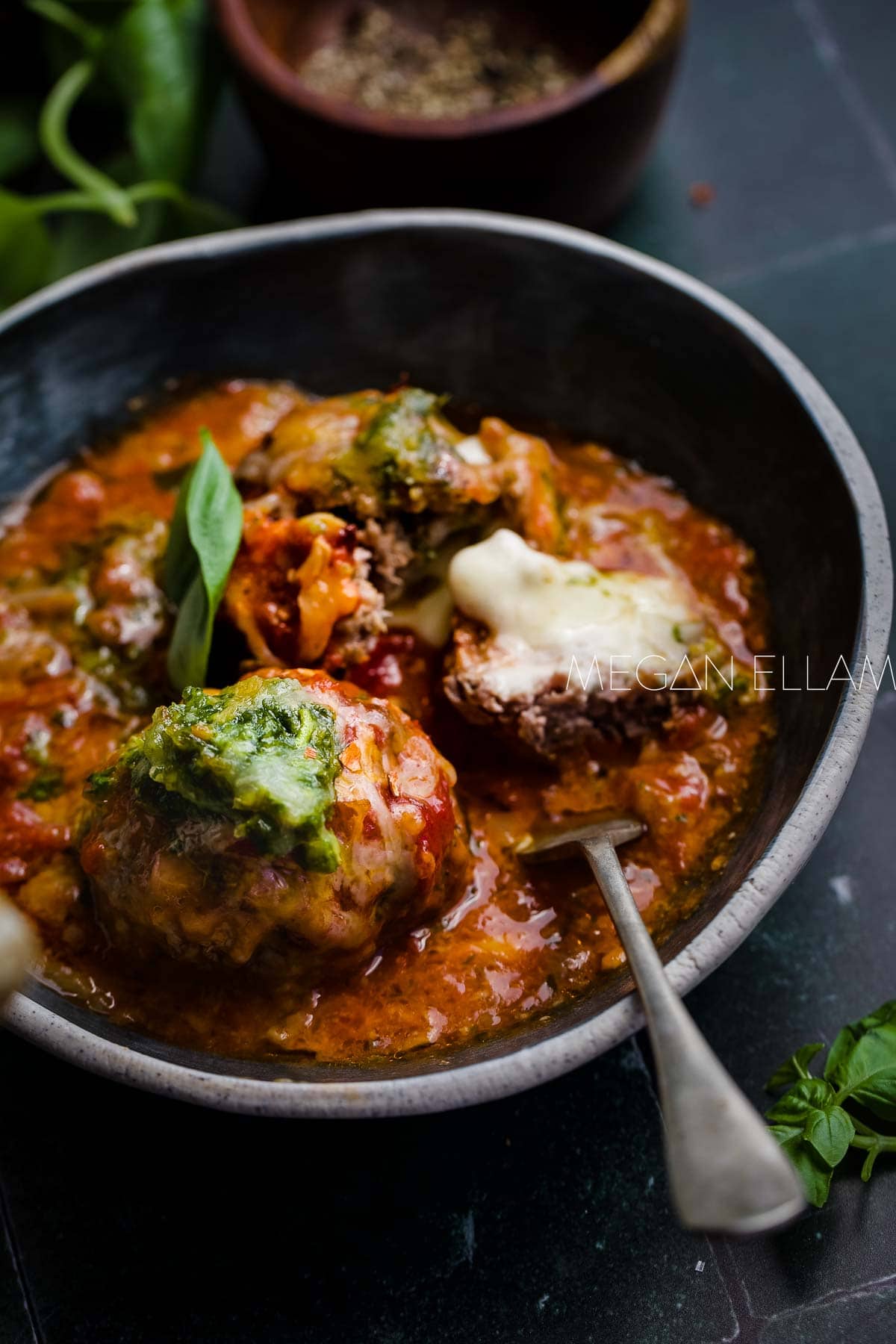 Meatballs i a bowl with a spoon and pesto.