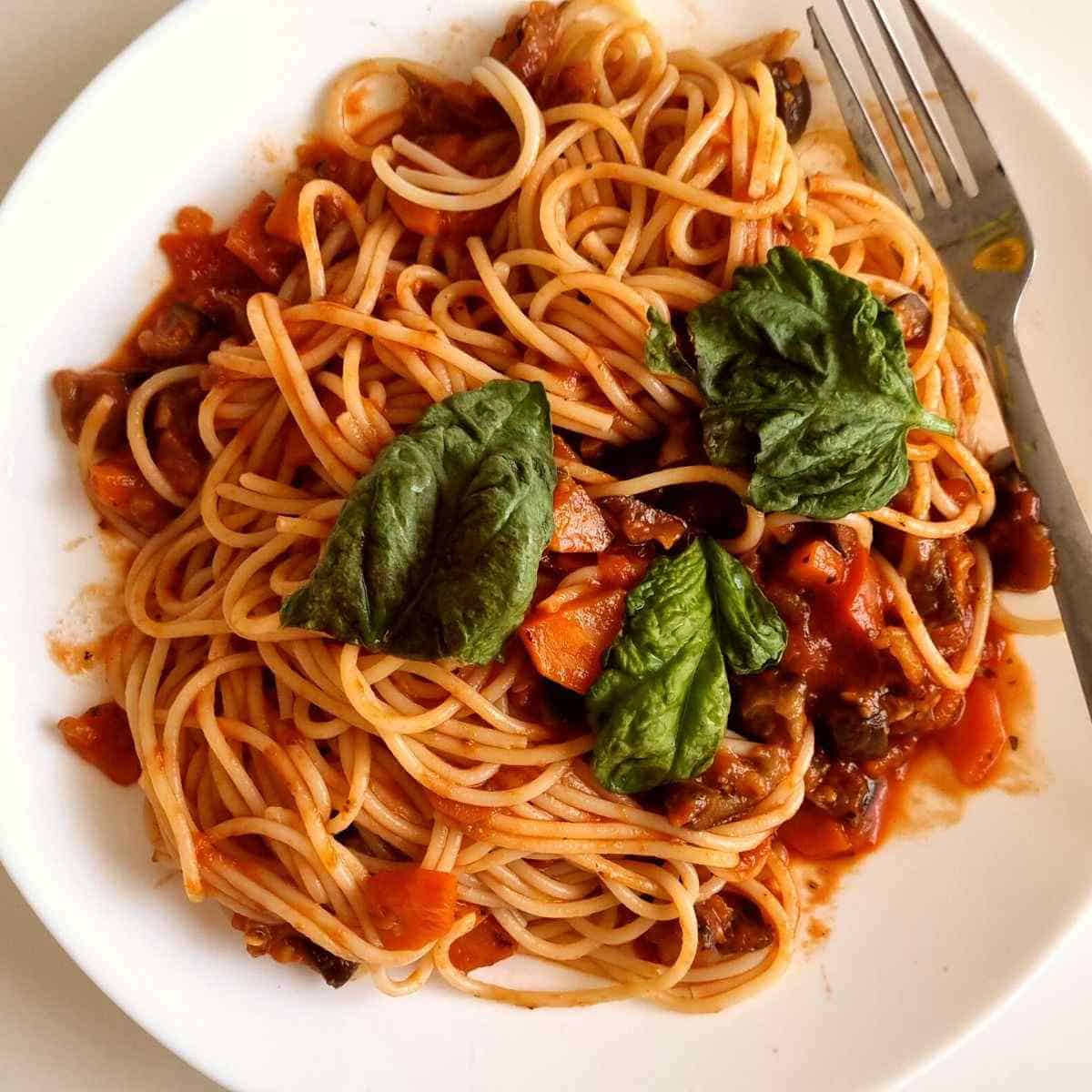 Pasta on a white plate with fresh basil on the top and a for on the side. 
